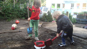 zwei Jungen häufeln Erde an die leicht herausschauende Kunststofftonne